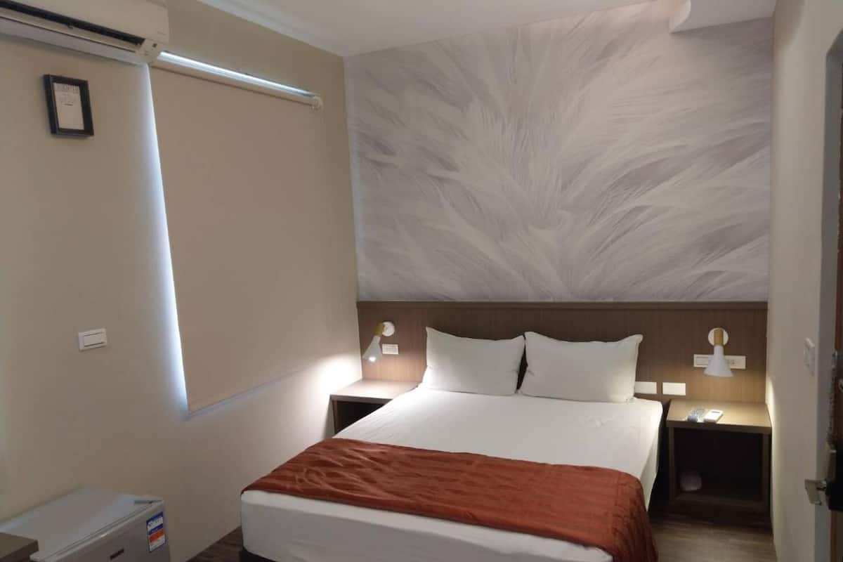 Habitación de hotel con una cama grande, una mesita de noche, un refrigerador pequeño y un aire acondicionado instalado en la pared.