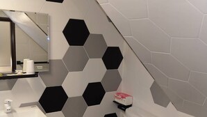 Une salle de bain moderne avec un lavabo blanc, des toilettes et un miroir au-dessus du lavabo. Les murs sont décorés de carreaux hexagonaux noirs et blancs.