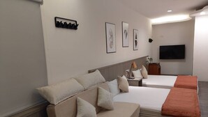 Une chambre d’hôtel équipée d’un canapé-lit, d’un lit simple, d’une télévision et d’œuvres d’art encadrées au mur.