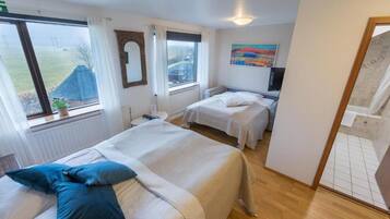 Habitación de hotel con dos camas, una ventana con vistas, un cuadro en la pared y un baño visible a través de una puerta abierta.