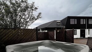Boblebad i en baghave med et træhegn, et moderne hus og en overskyet himmel.