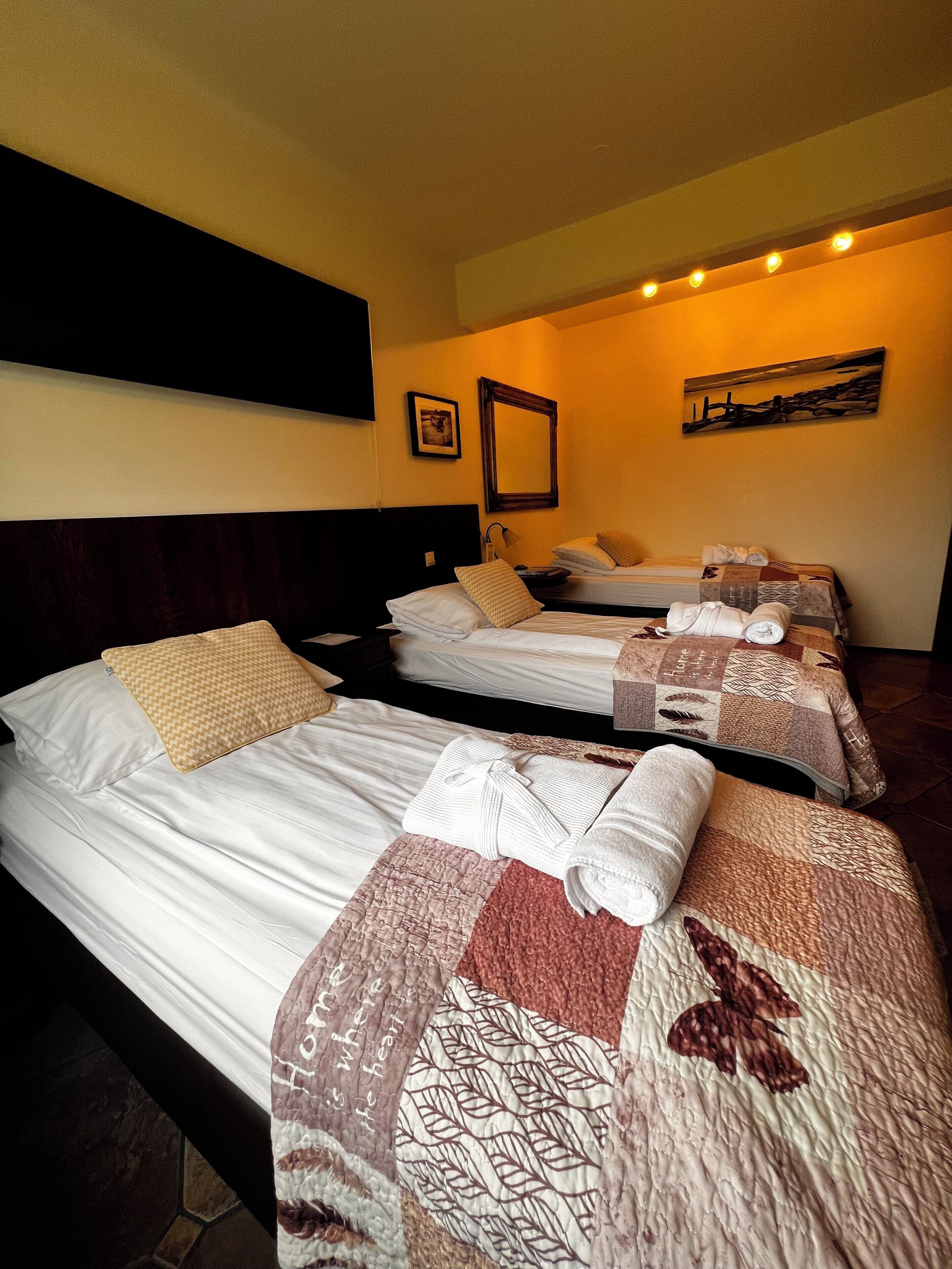 Ein Hotelzimmer mit drei Betten, jedes mit einer unterschiedlich gemusterten Tagesdecke.