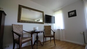 Et værelse med to træstole, et rundt bord, et stort spejl, et fladskærms-tv og et billede i ramme på væggen.
