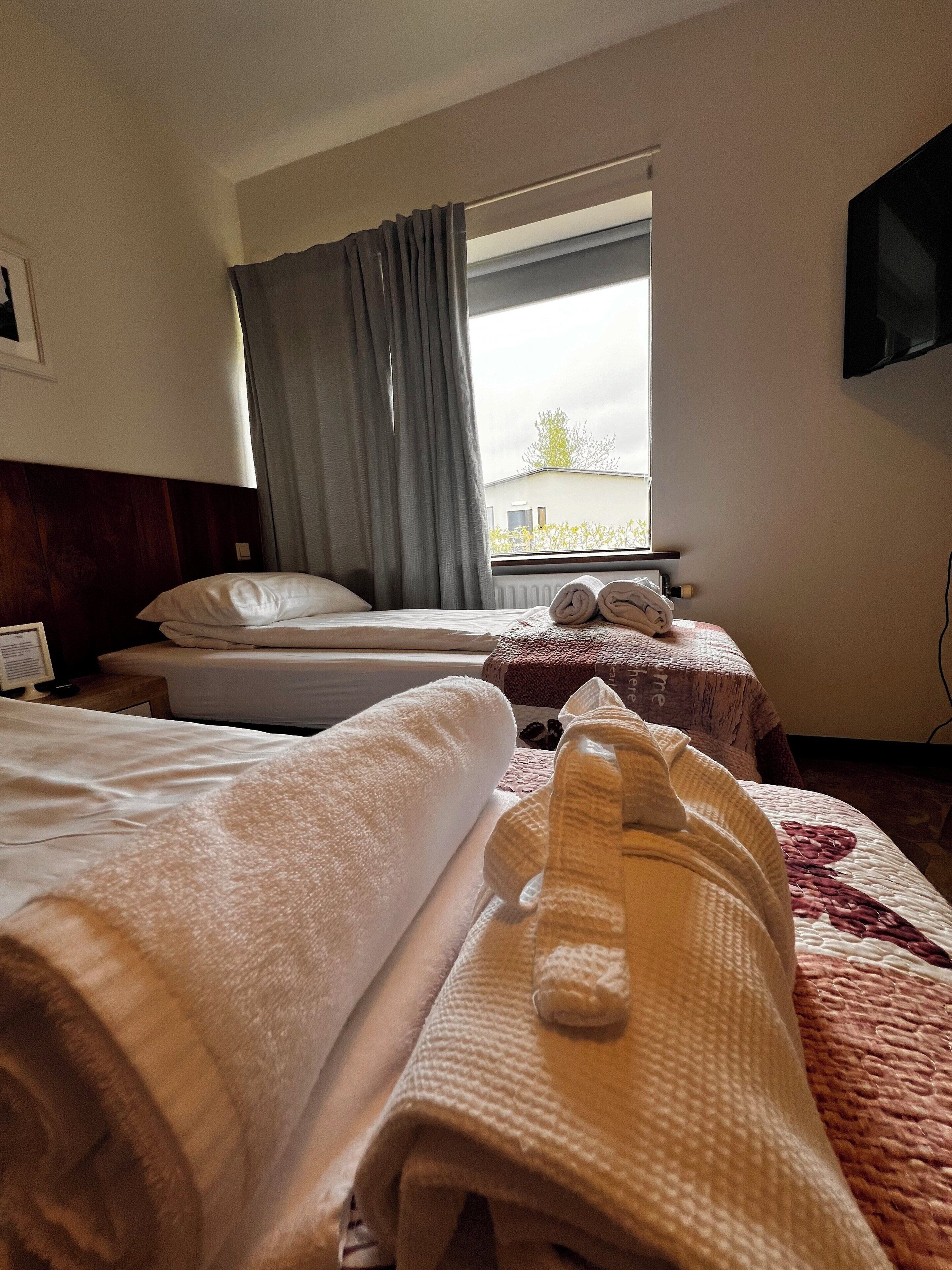 Une chambre d’hôtel avec deux lits, une fenêtre avec des rideaux, un téléviseur à écran plat fixé au mur et une vue sur l’extérieur.