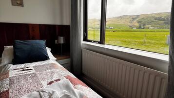 A bedroom with a large window, a bed with a patterned quilt, a radiator, and a view of a green landscape.