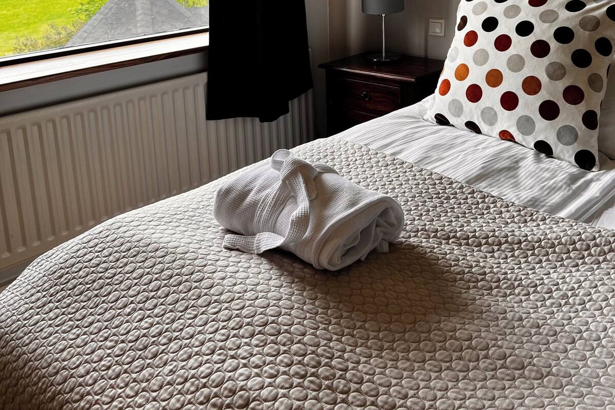 A neatly made bed with a quilted cover, a pillow with a polka dot pattern, and a folded towel on the bed.