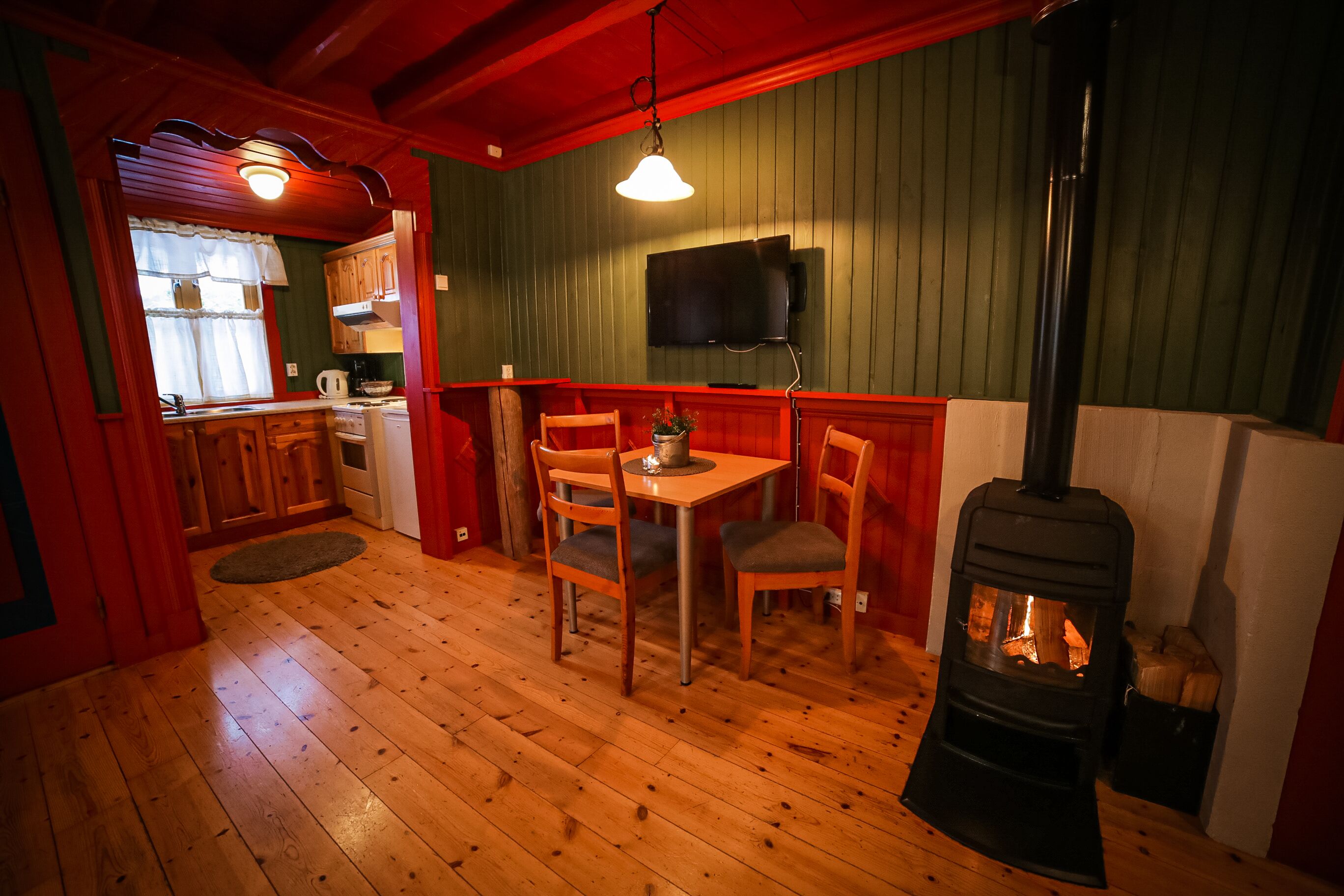 A cozy cabin interior with a dining area, wooden floors, a fireplace, and a television mounted on the wall.