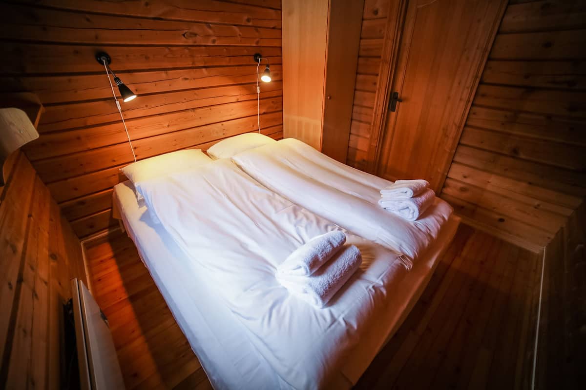A wooden cabin bedroom with two beds, each with white linens and towels, and a ceiling light fixture.