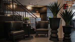 A modern interior with a staircase, leather armchairs, and large potted plants.