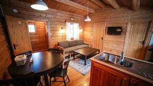 A cozy cabin interior with a dining table, chairs, a sofa, a kitchen area with a sink, and a television mounted on the wall.