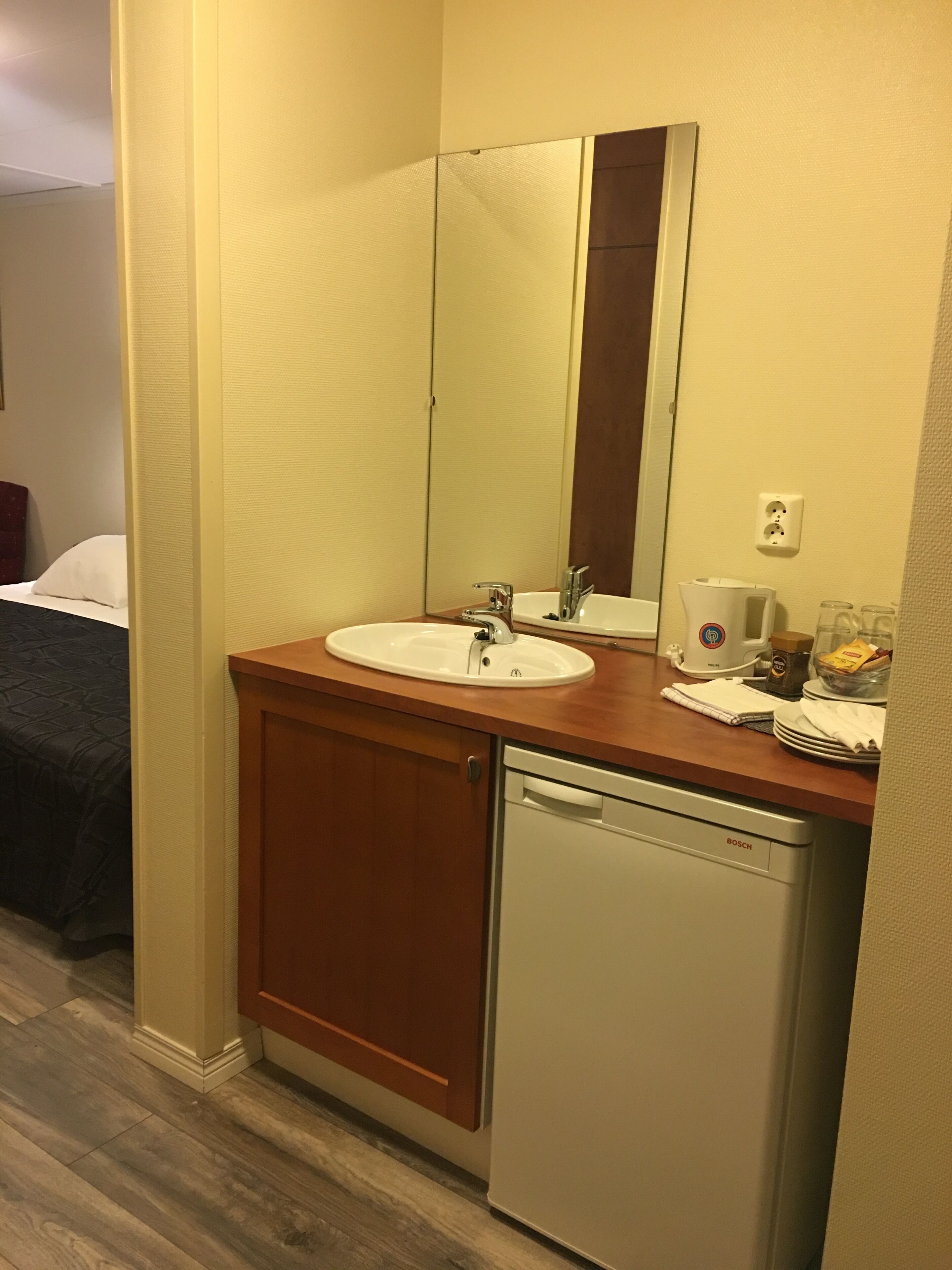 Casa de banho de hotel com lavatório, espelho e máquina de lavar loiça Bosch.