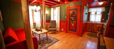 Um quarto aconchegante com piso de madeira, um sofá vermelho, uma mesa de jantar e uma área de cozinha com janela.