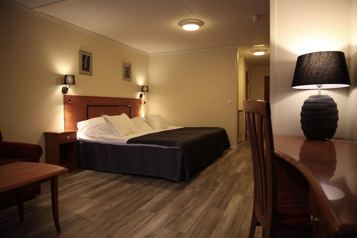 A hotel room with a bed, bedside tables, a desk, and a lamp.
