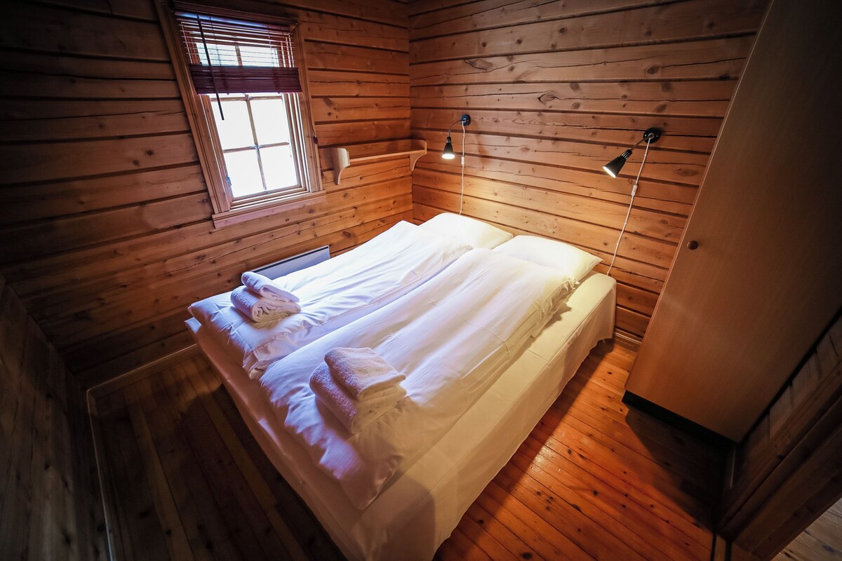Una habitación de cabaña de madera con una cama, una ventana y una lámpara fijada a la pared.