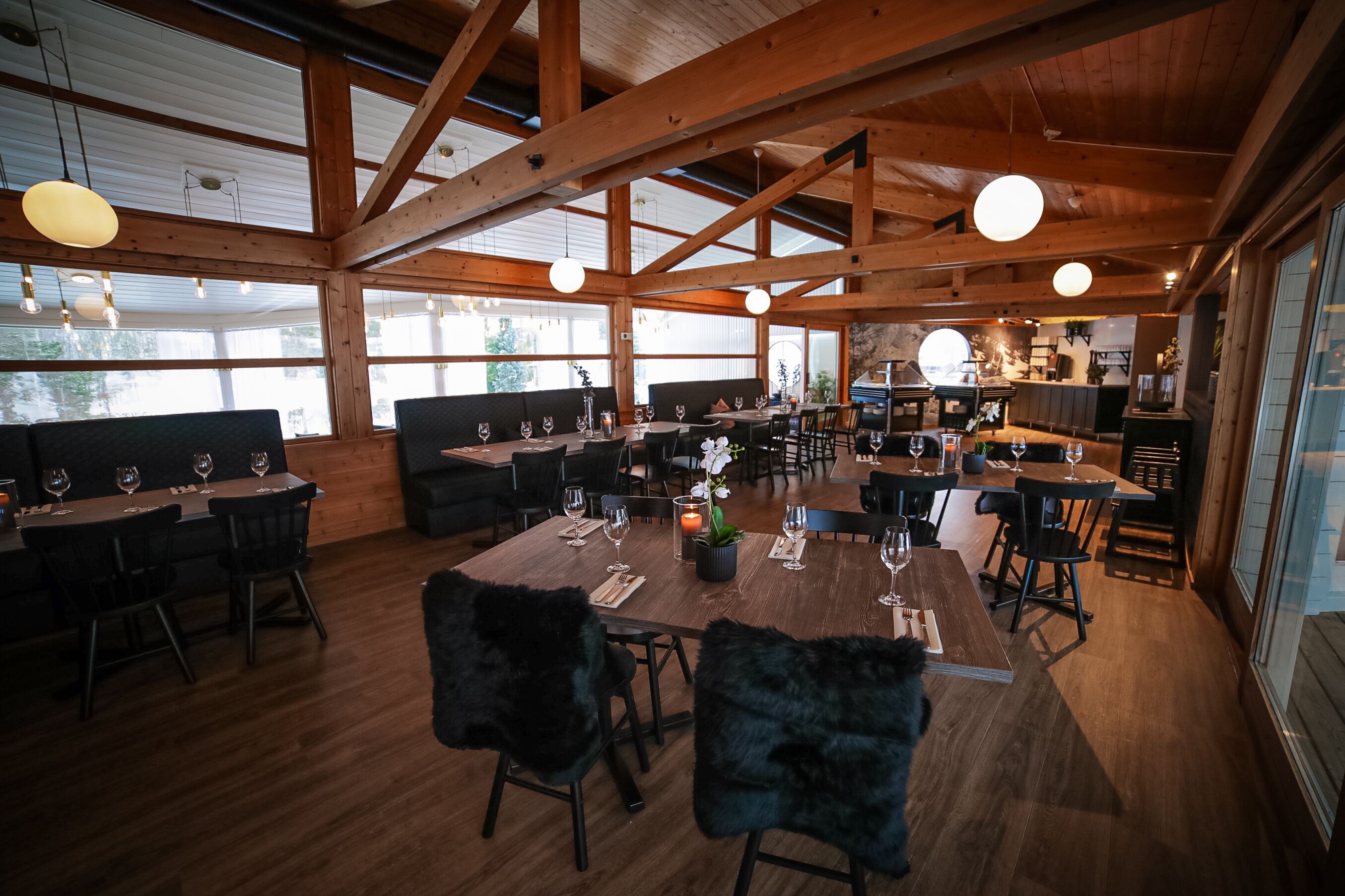 A spacious dining area with wooden beams, large windows, and multiple tables set for dining.