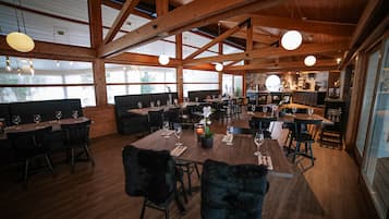 Un comedor espacioso con vigas de madera, ventanas amplias y varias mesas dispuestas para comer.
