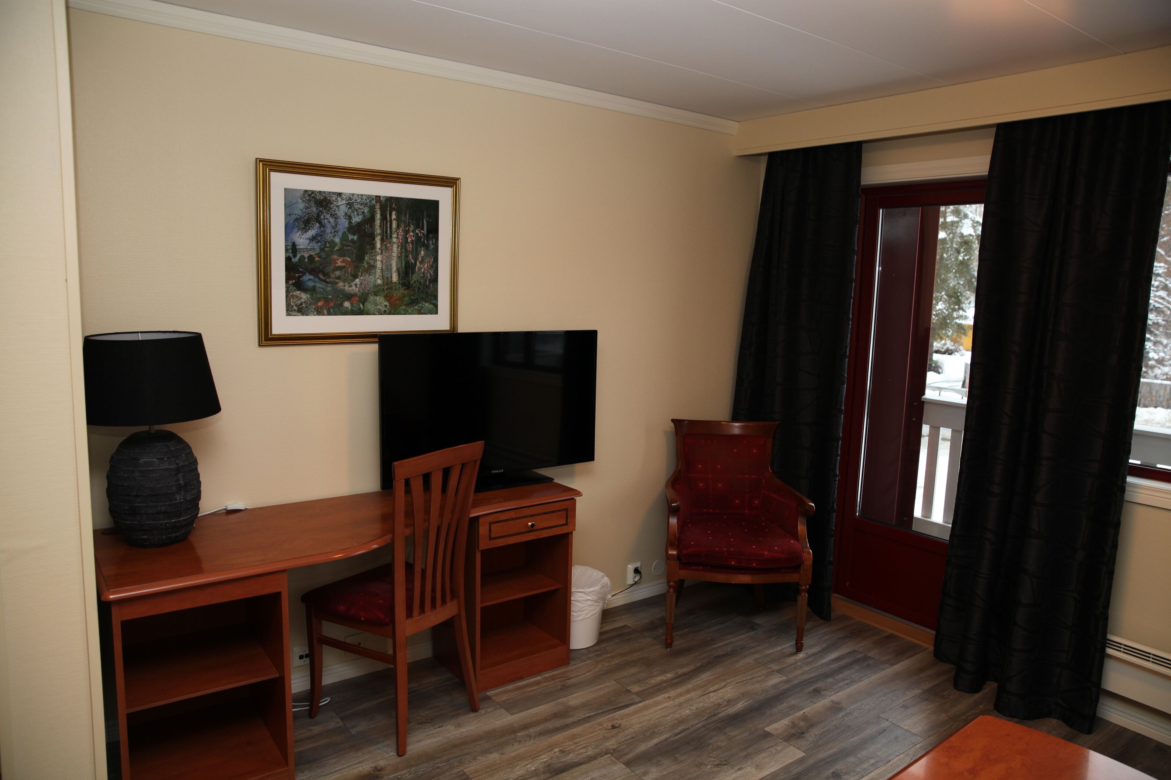 A room with a desk, chair, television, and a framed picture on the wall.