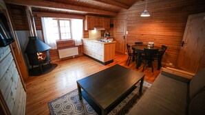A cozy cabin interior with a wood-burning stove, a dining area, and a kitchen.