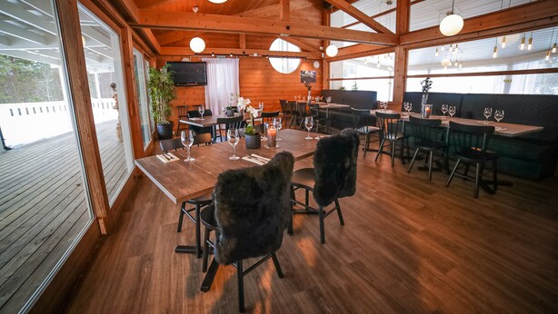 A wooden interior with tables and chairs, a television, and large windows.