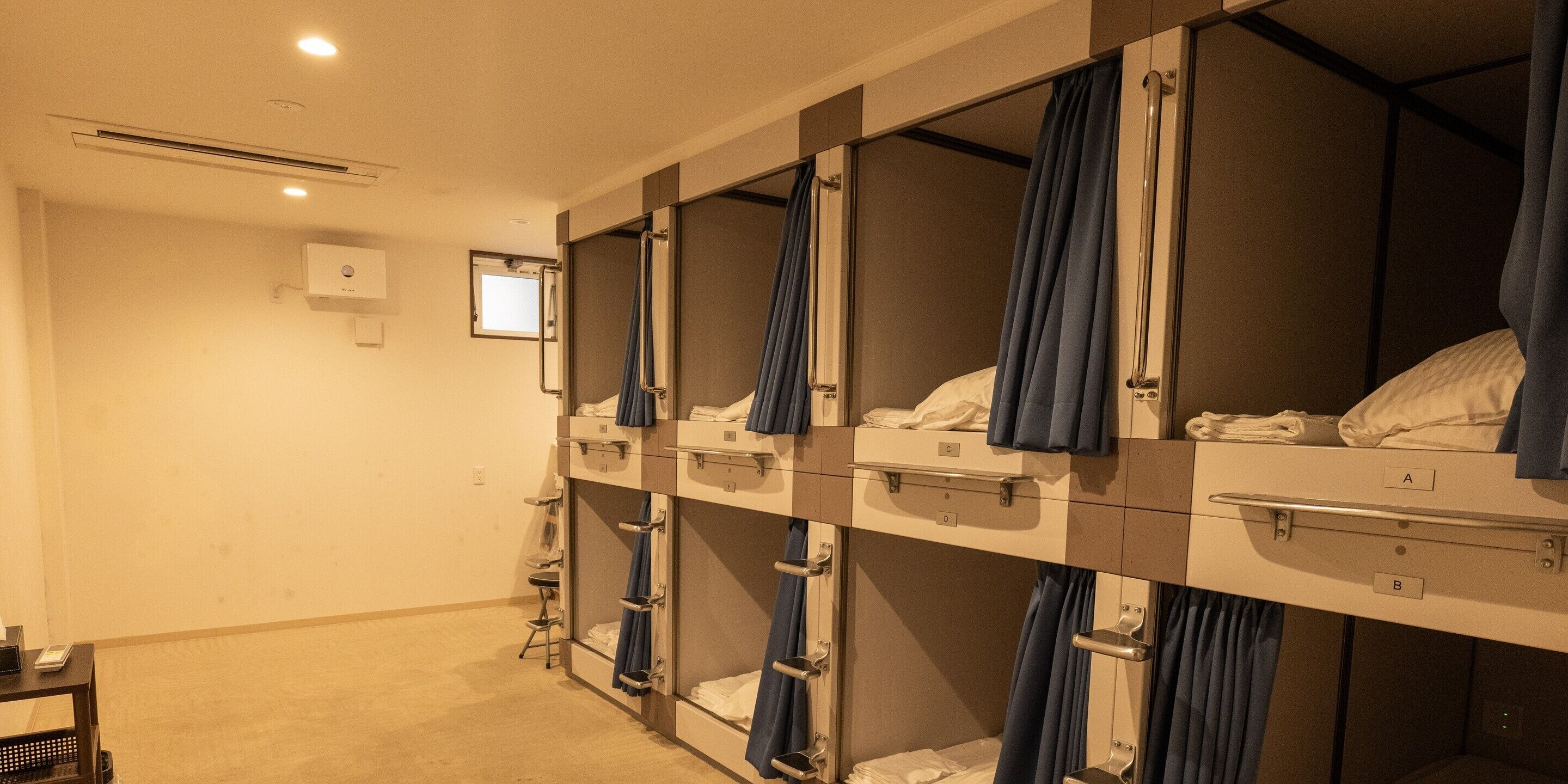 A hotel room with bunk beds, each with a curtain, a small table, and a chair.