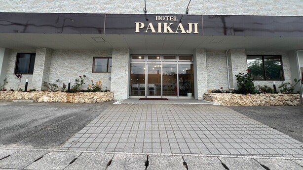 Hotel Paikaji, met een stenen gevel, grote glazen ingang en een betegelde looppad naar de ingang.