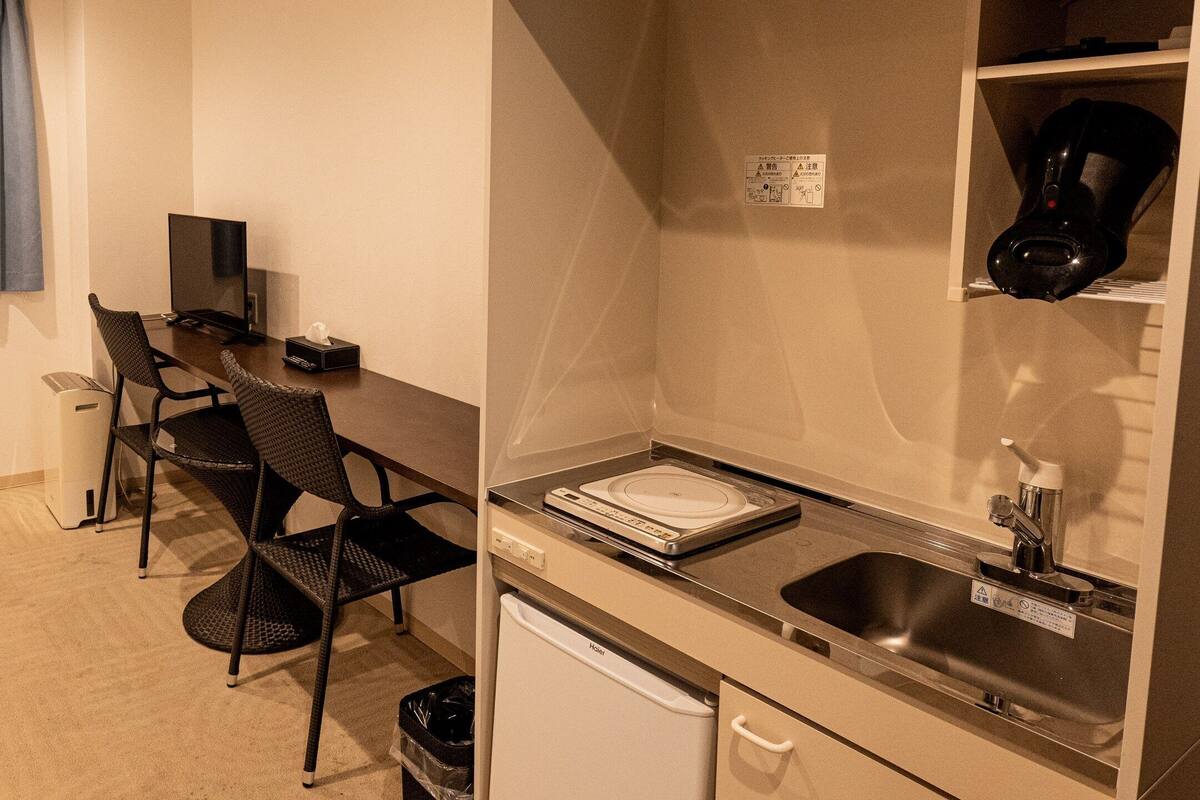 Una kitchenette compacta con un lavamanos, una cafetera y un refrigerador pequeño.