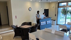 Een hotel receptie met een receptiebalie, twee medewerkers, een klok en uitzicht op het omliggende landschap door grote ramen.