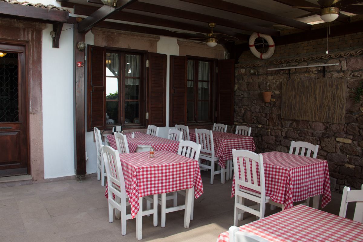 Eine Terrasse im Freien mit weißen Tischen und Stühlen, bedeckt mit rot-weißen karierten Tischdecken.
