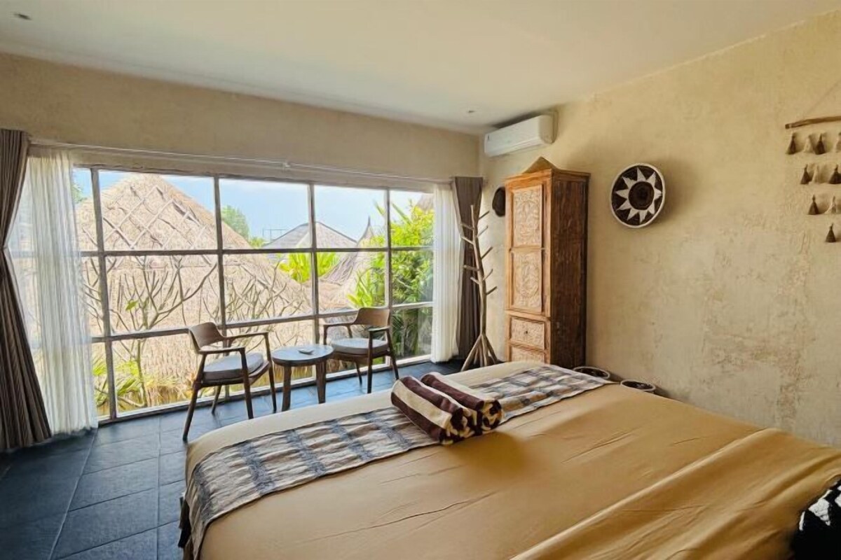 A hotel room with a large bed, a dining table, and chairs by a large window.
