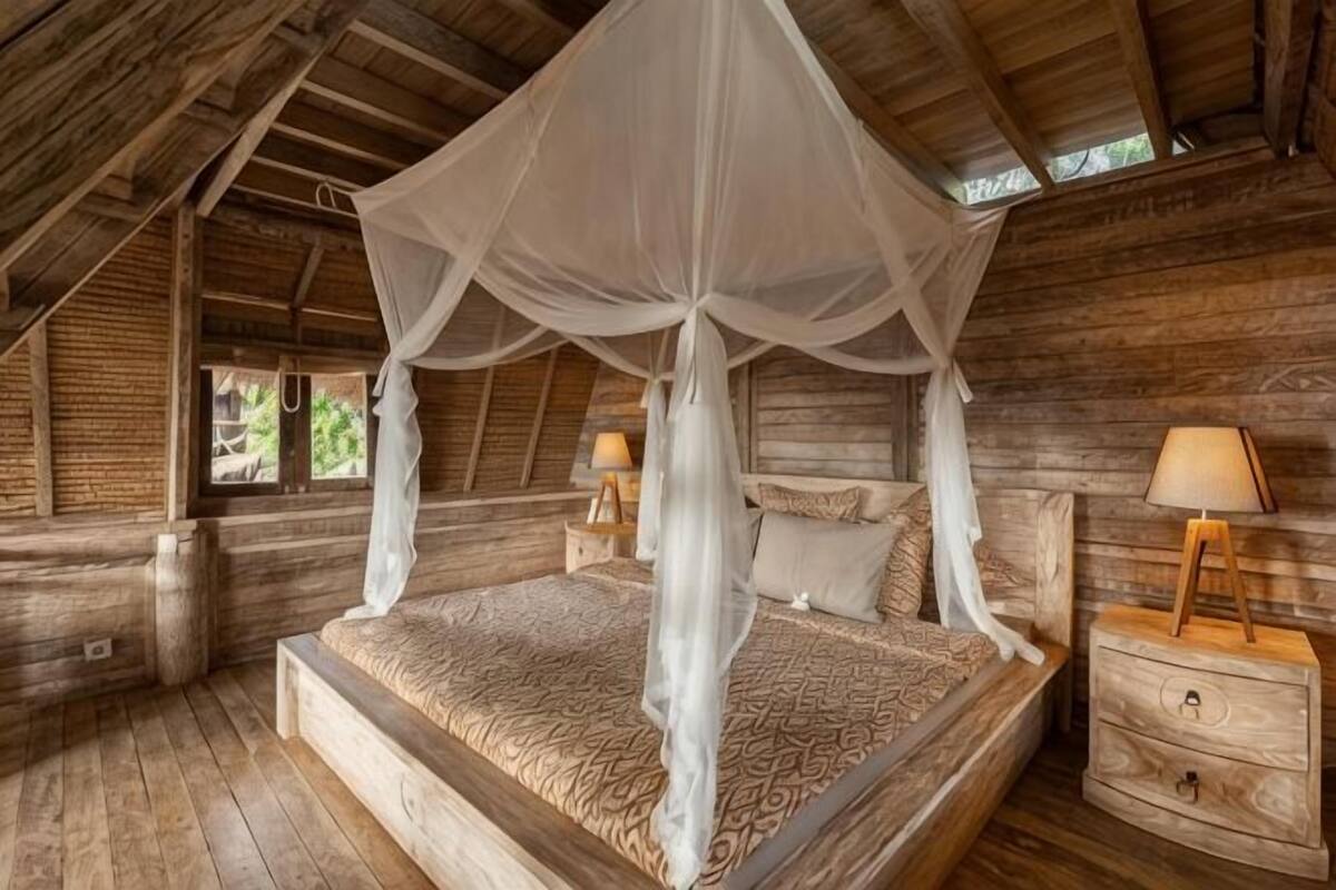Una habitación de madera con una cama con dosel, una mesita de noche y una lámpara.