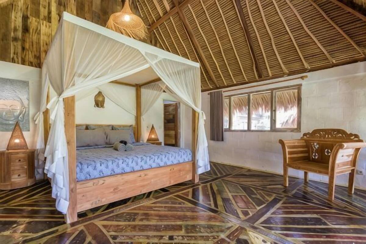 Una habitación con cama con dosel, un banco de madera y suelo estampado.