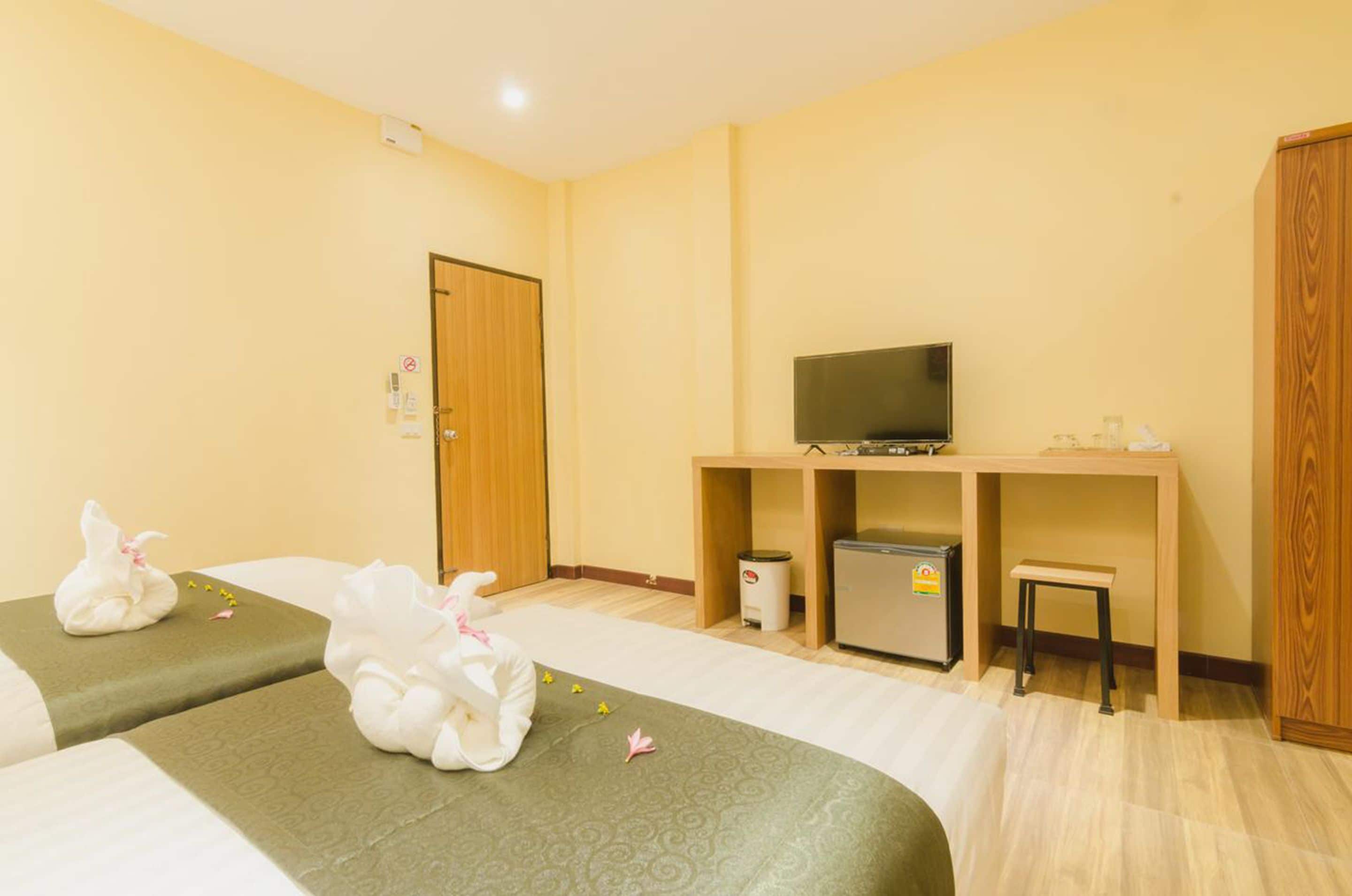 A hotel room with two beds, a television, a small refrigerator, and a wooden wardrobe.