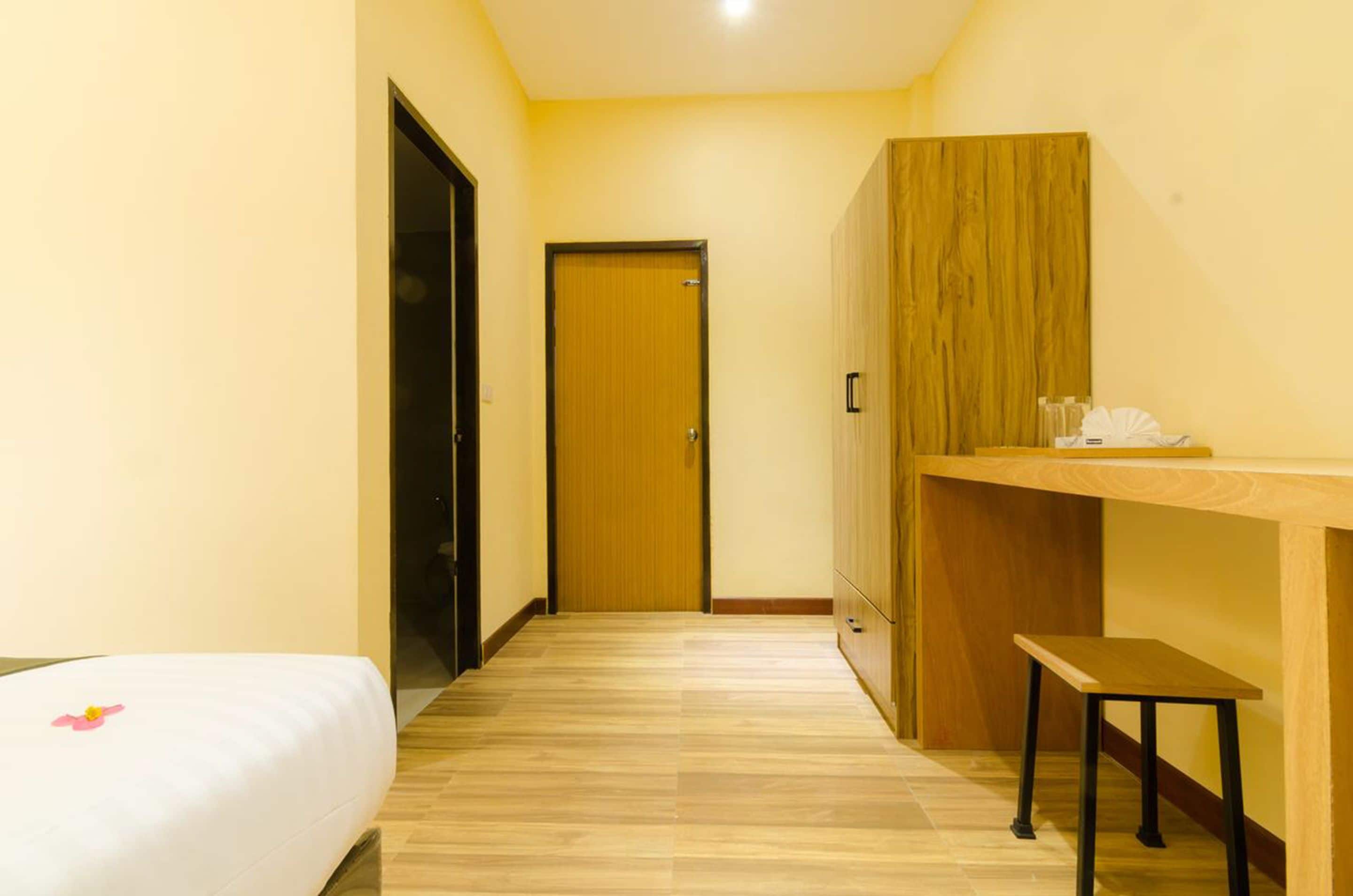 A hotel room with a wooden floor, a bed with a white cover, a wooden wardrobe, and a small wooden table.