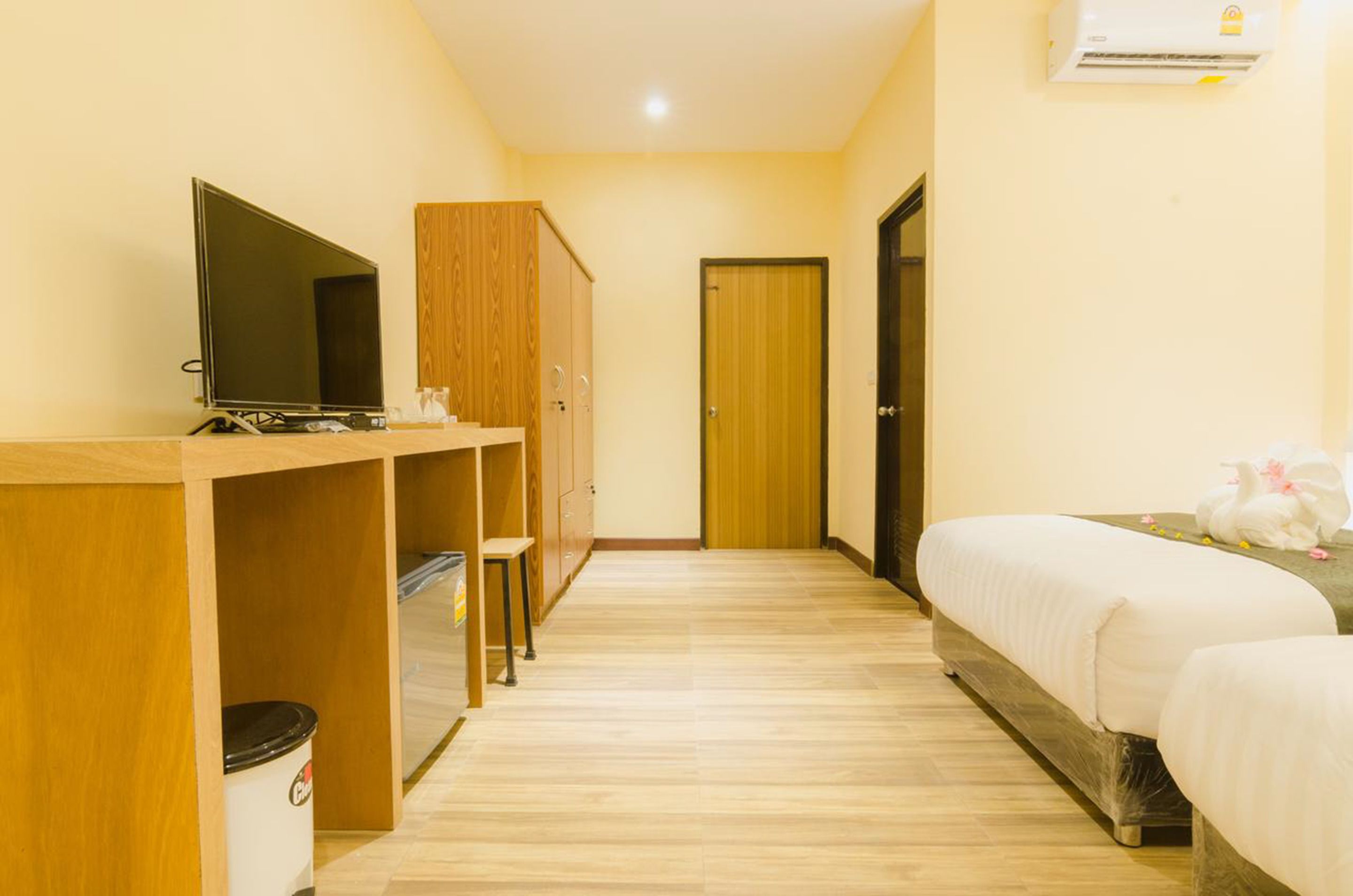A hotel room with a wooden desk, a television, a wardrobe, a bed, and an air conditioning unit.
