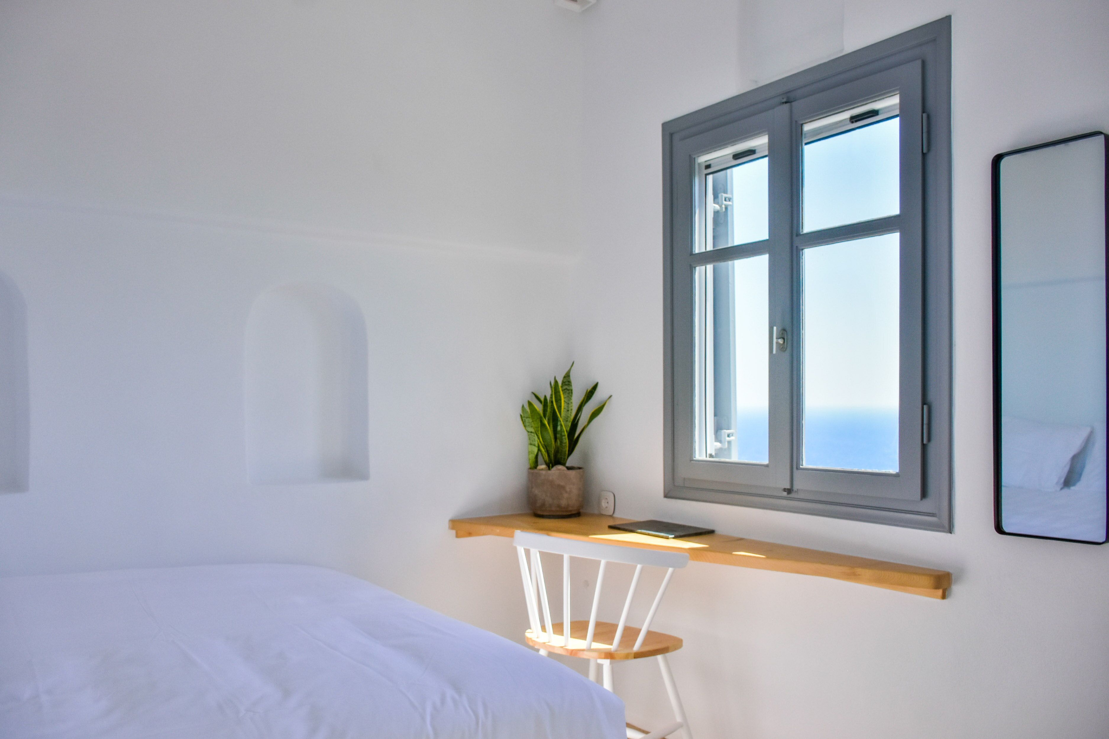Un dormitorio con cama, escritorio con computadora portátil, planta en maceta y ventana con vista.