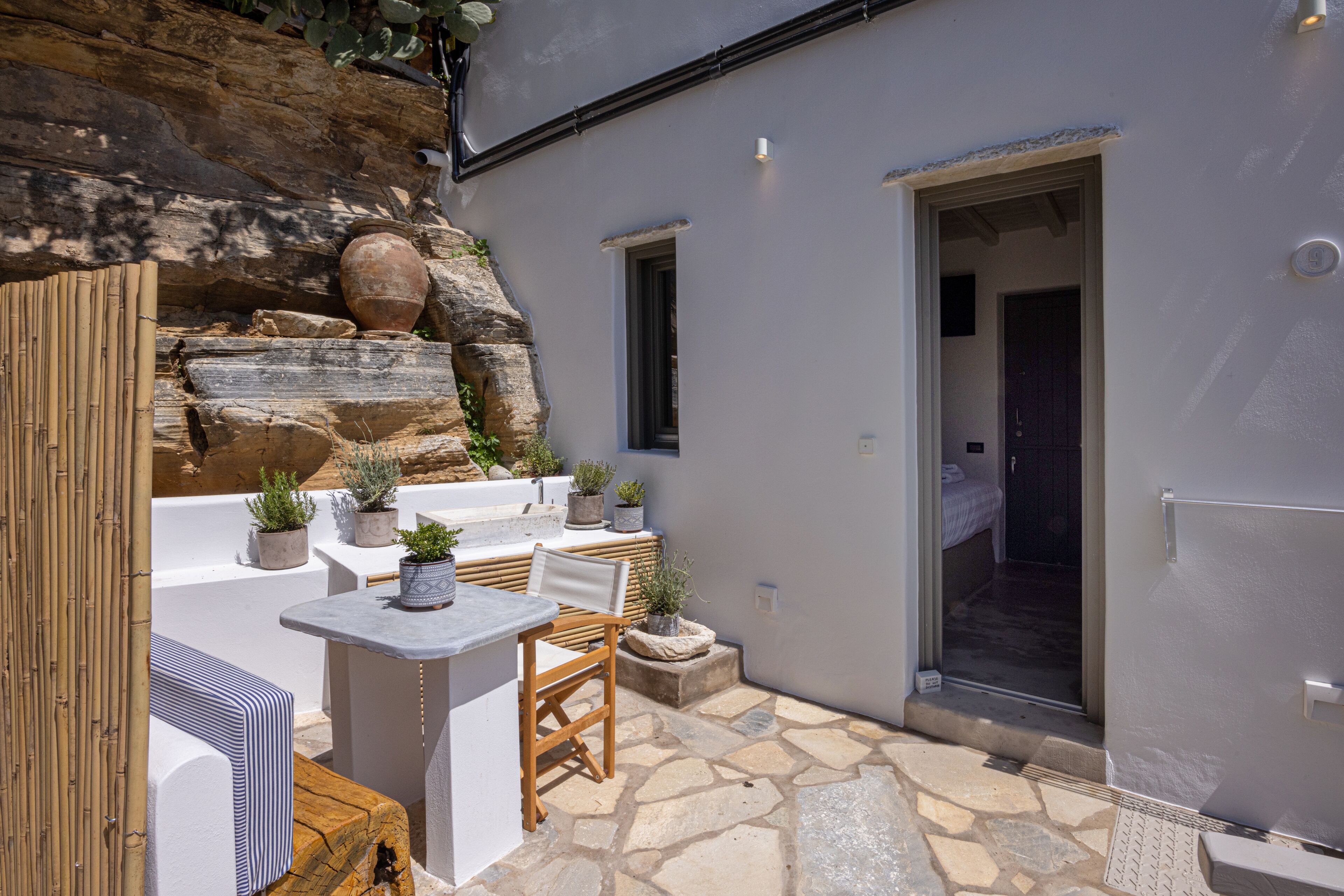 A patio area with a stone floor, white furniture, potted plants, and a view of a rocky landscape.