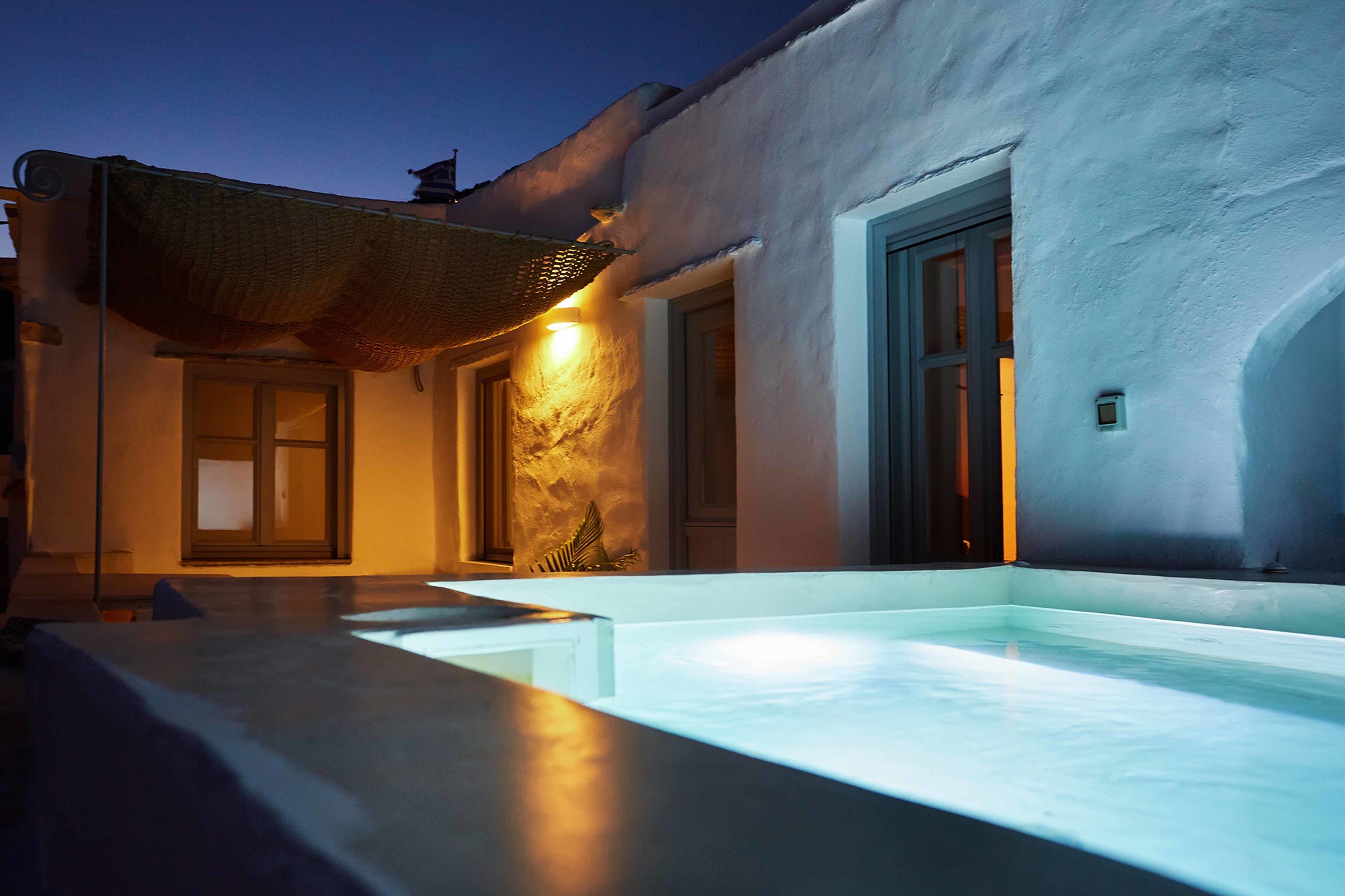 A modern outdoor pool area with a stone wall and a door, illuminated by warm lighting.