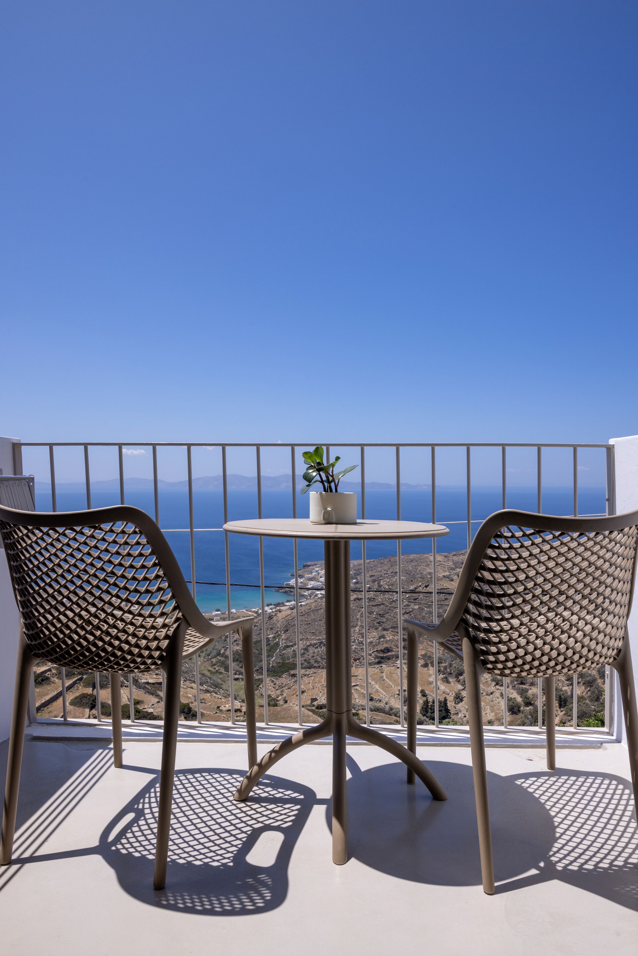 A balcony with two chairs and a small table, overlooking a coastal landscape.