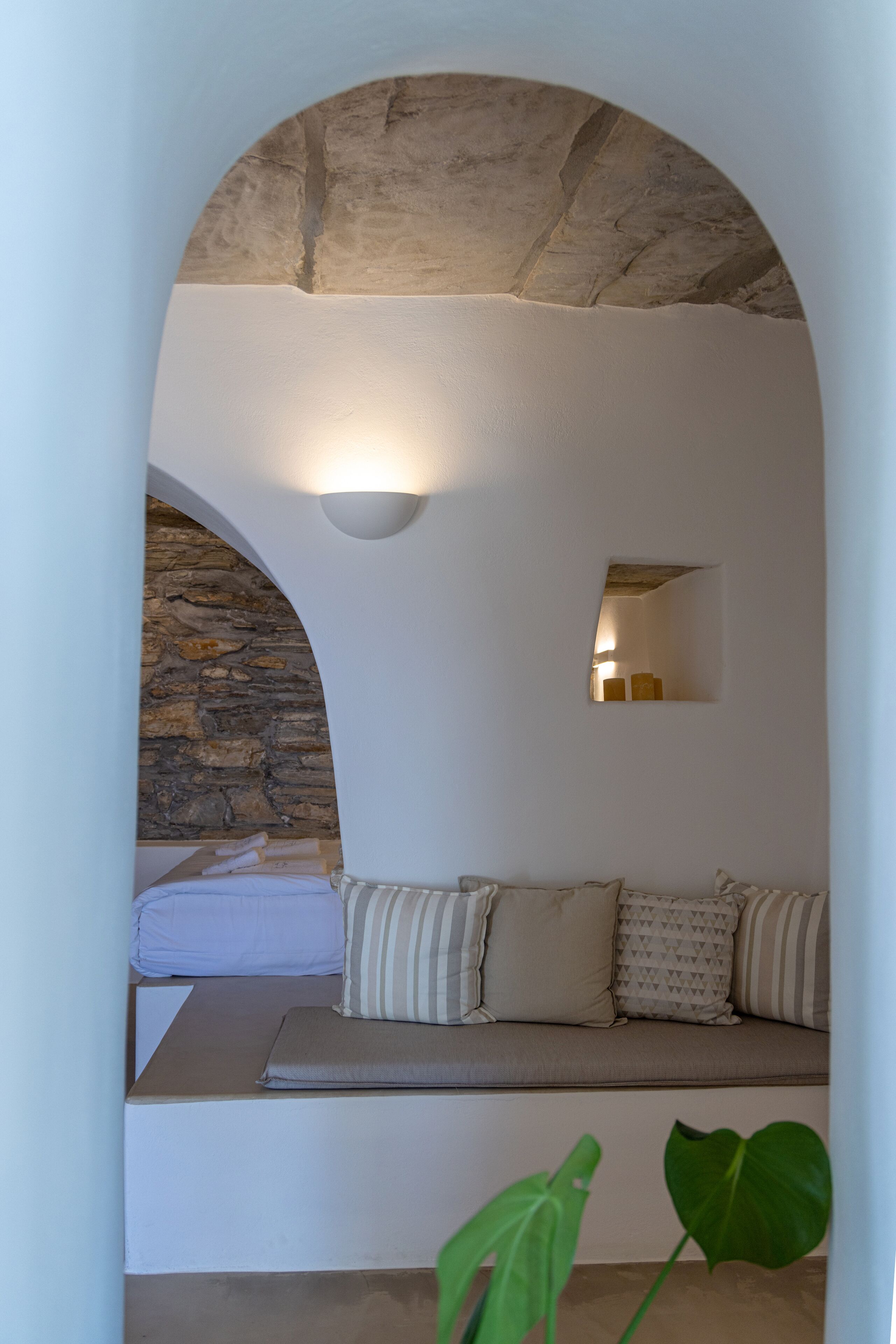 Una habitación acogedora con pared de piedra, un banco con cojines, un espejo pequeño e iluminación de pared.