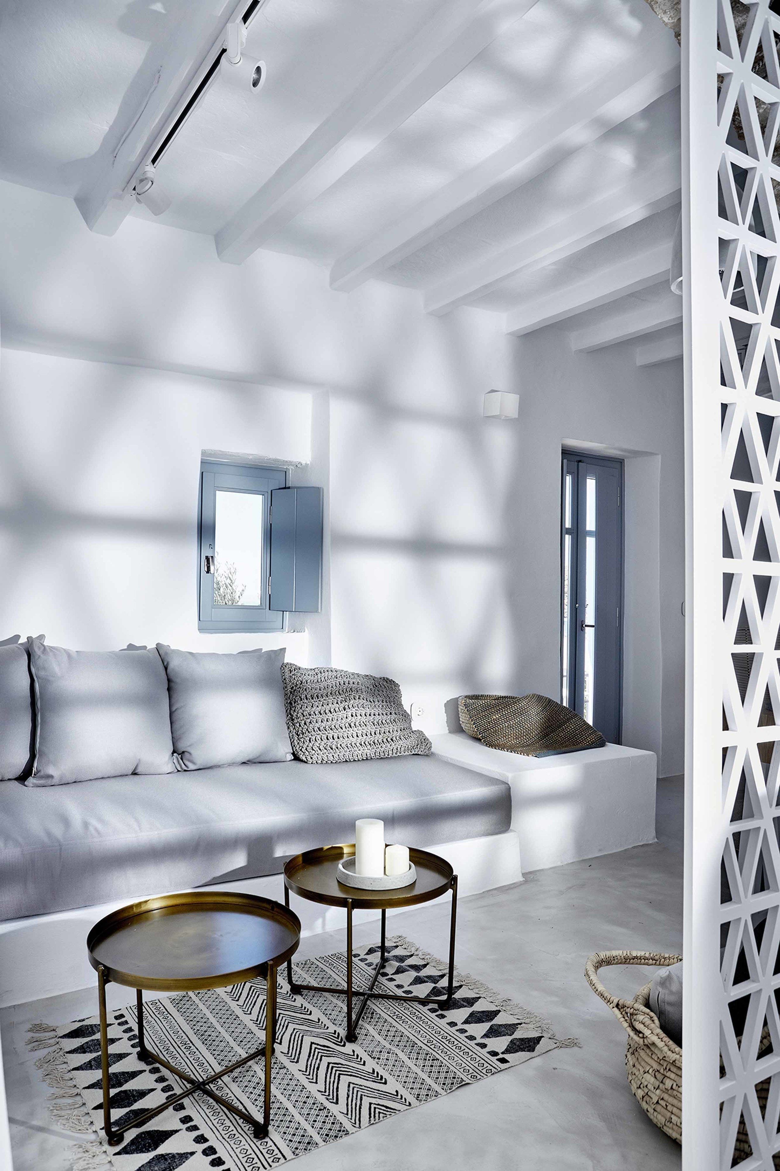 Un salon moderne avec un canapé blanc, deux petites tables rondes et un tapis à motifs.