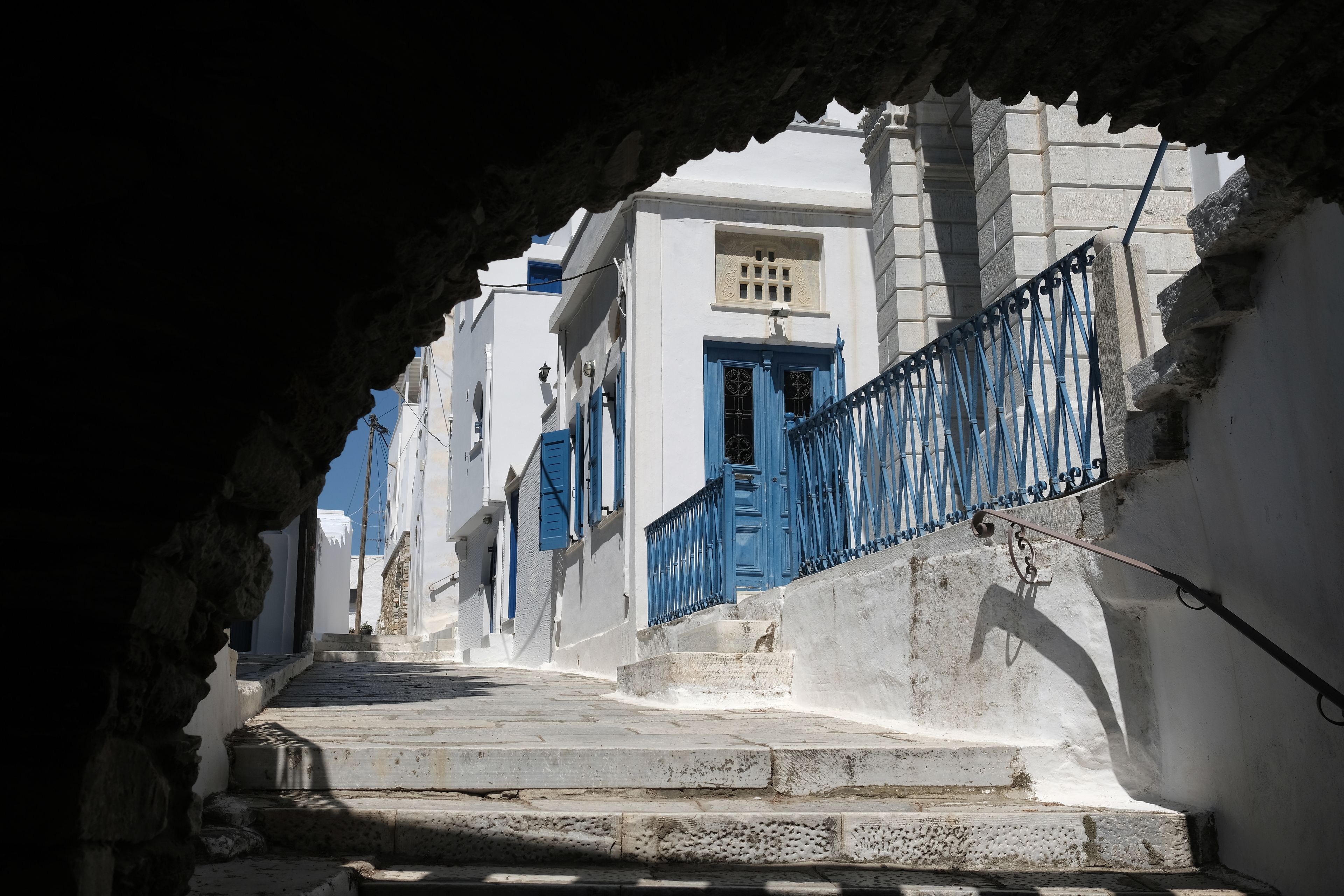 A narrow street with white buildings and blue doors, leading up a set of stone steps.