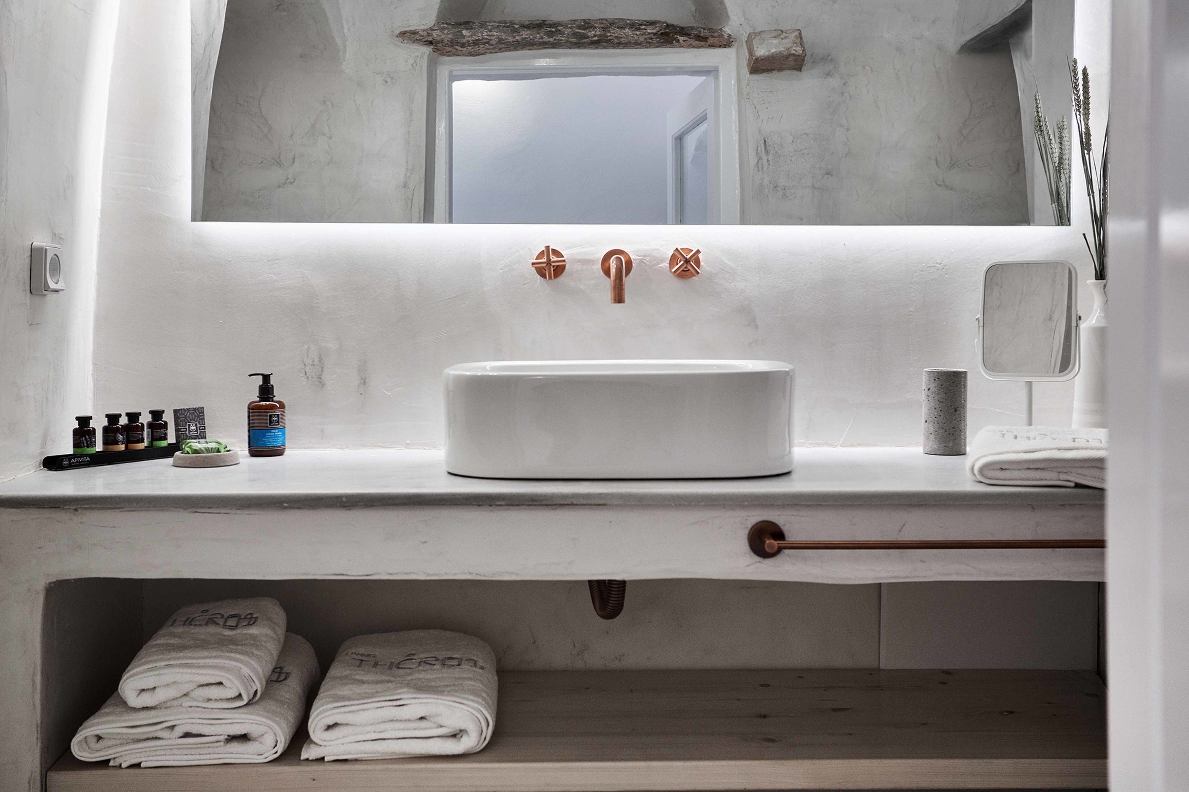 Une salle de bain avec un lavabo blanc, des robinets en cuivre, un miroir et des serviettes soigneusement pliées.