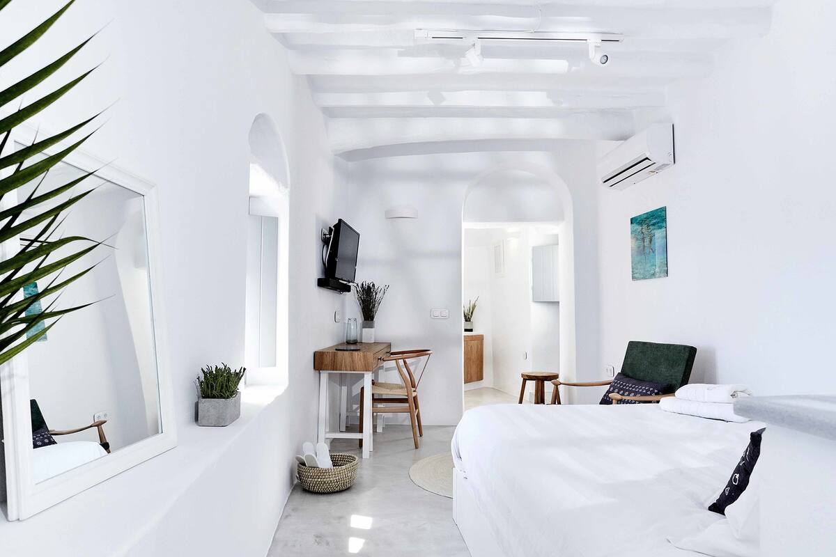 Een moderne, minimalistisch ingerichte slaapkamer met een groot bed, een bureau en een stoel.