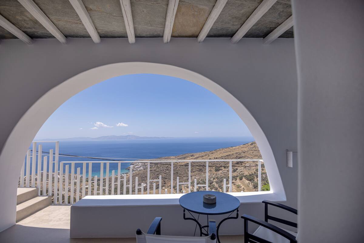 Een balkon met een witte reling, een tafel en uitzicht op zee en heuvels.