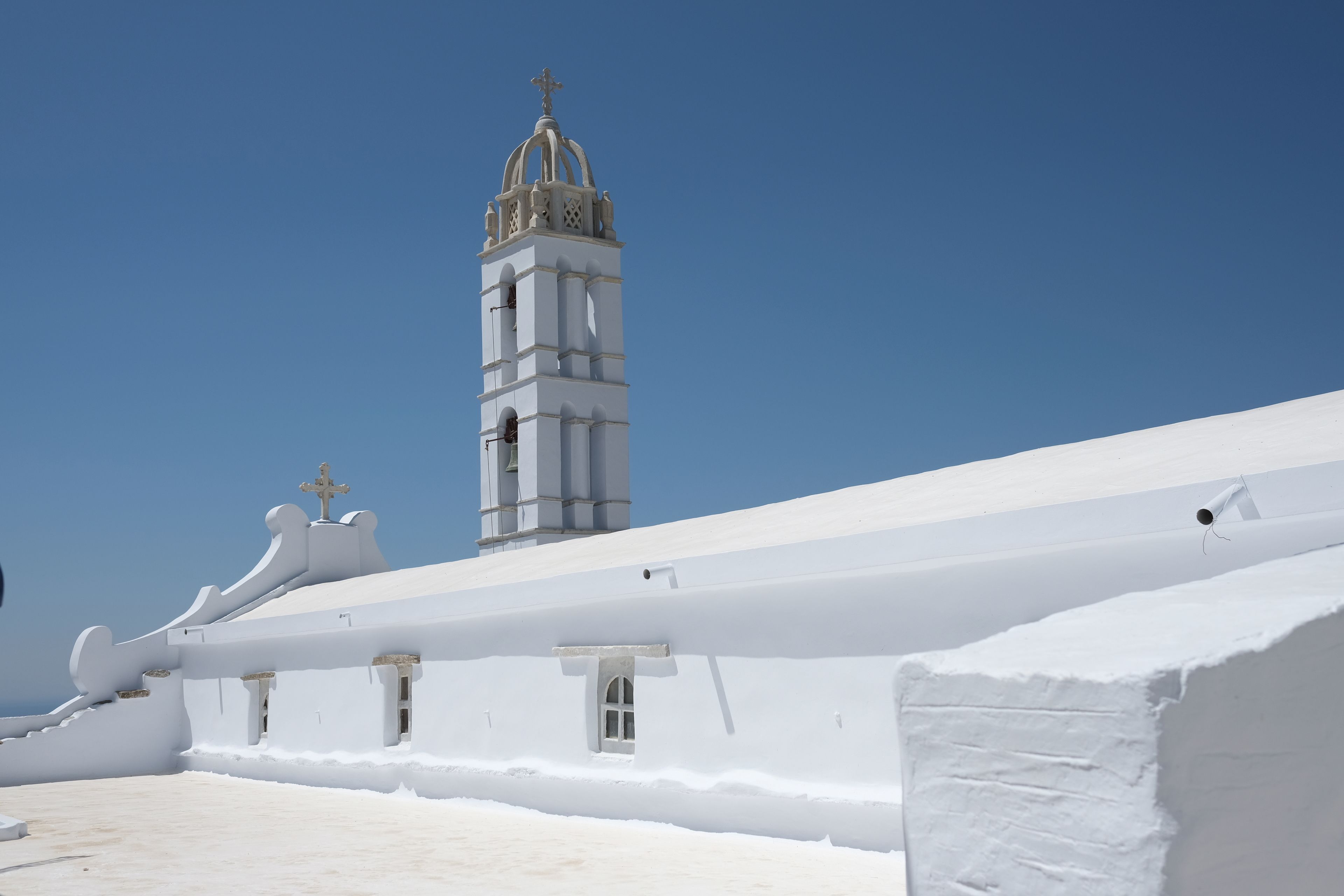 A white building with a tall tower and a cross on top.