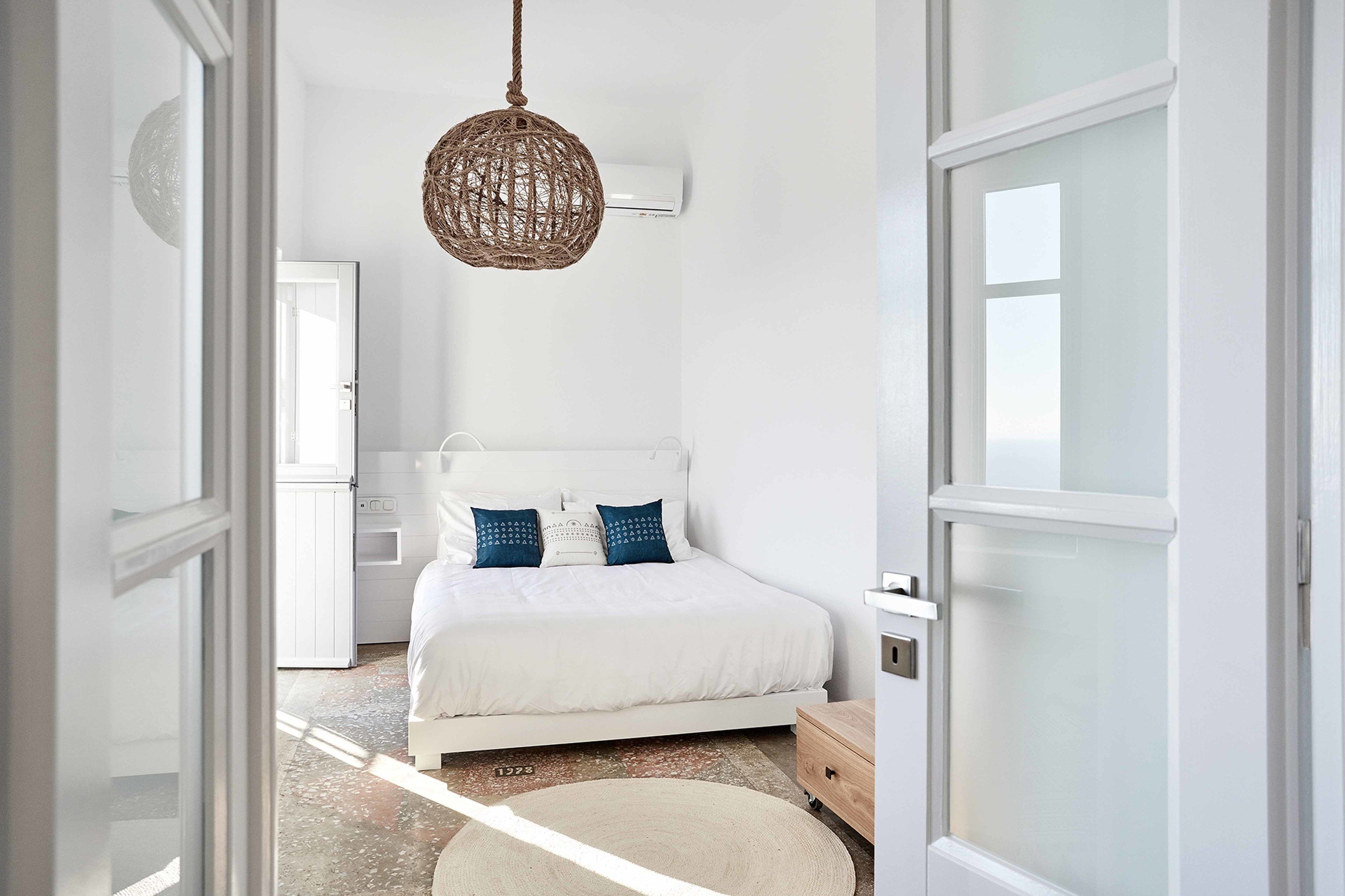 Quarto com cama branca, luminária de tecido e unidade de ar condicionado branca.