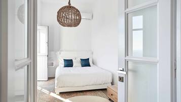 Quarto com cama branca, luminária de tecido e unidade de ar condicionado branca.
