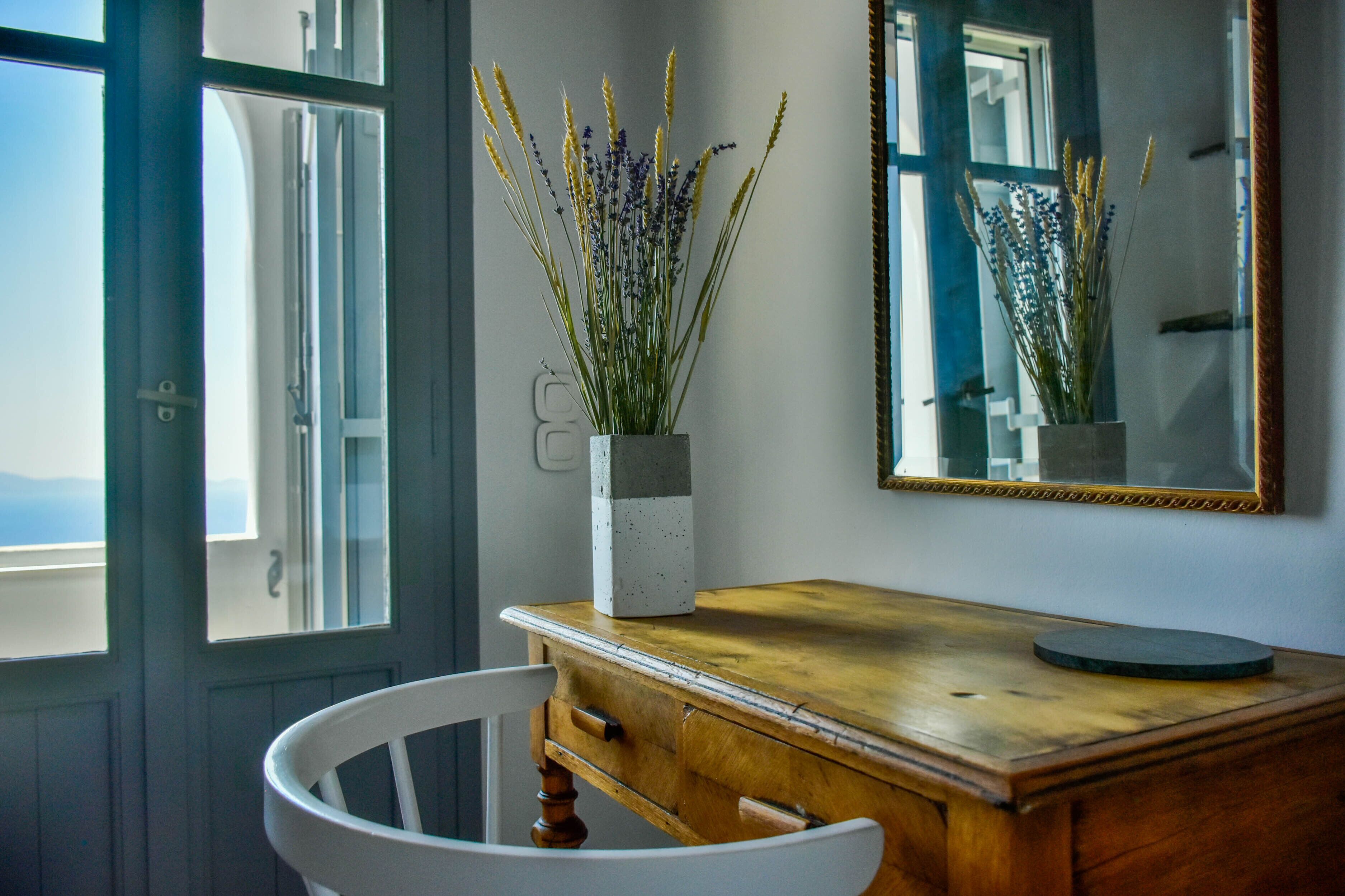 Une pièce comprenant une commode en bois, une chaise blanche et un vase contenant des plantes séchées, posé sur la commode.