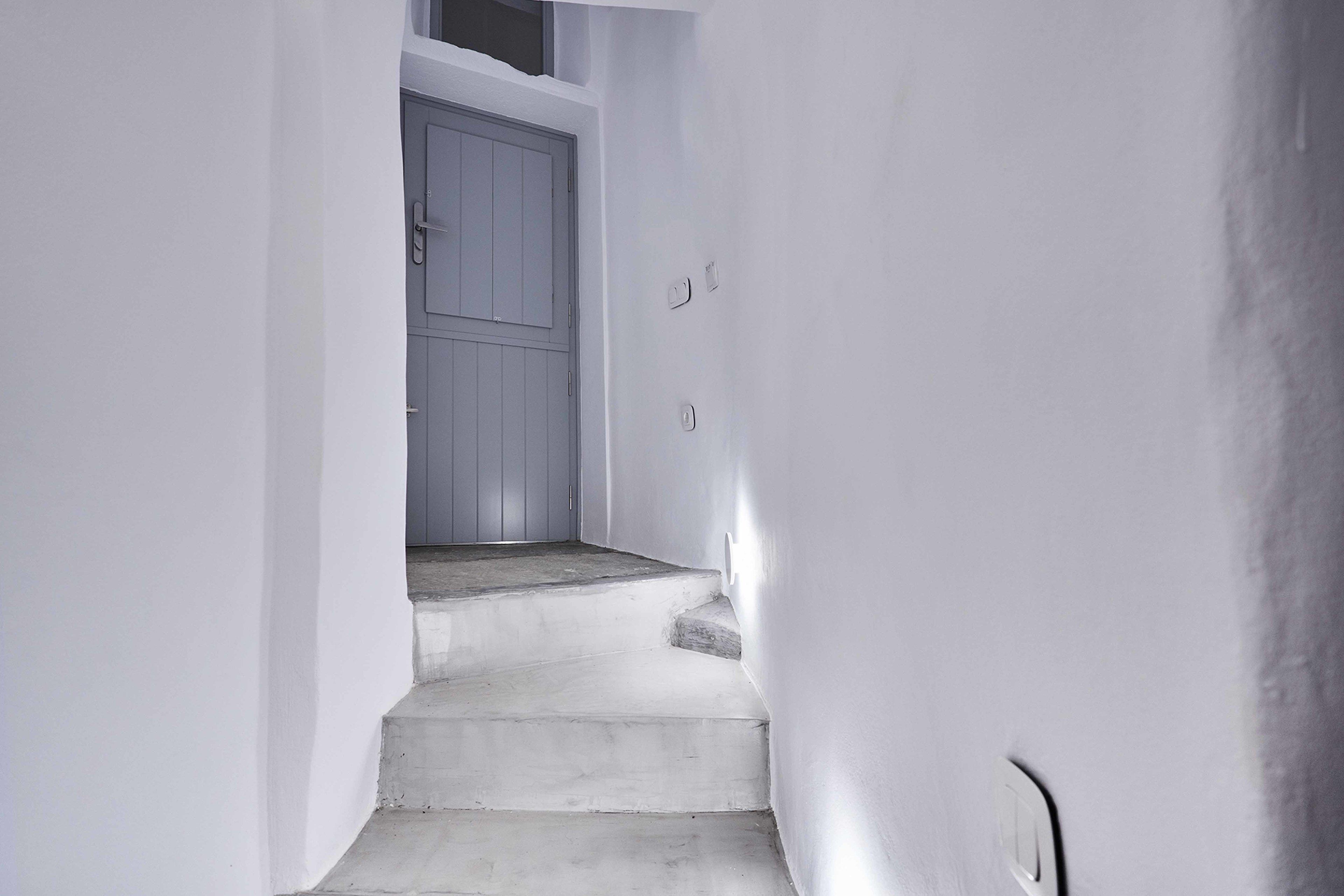 A narrow, white-walled stairway leading to a door.