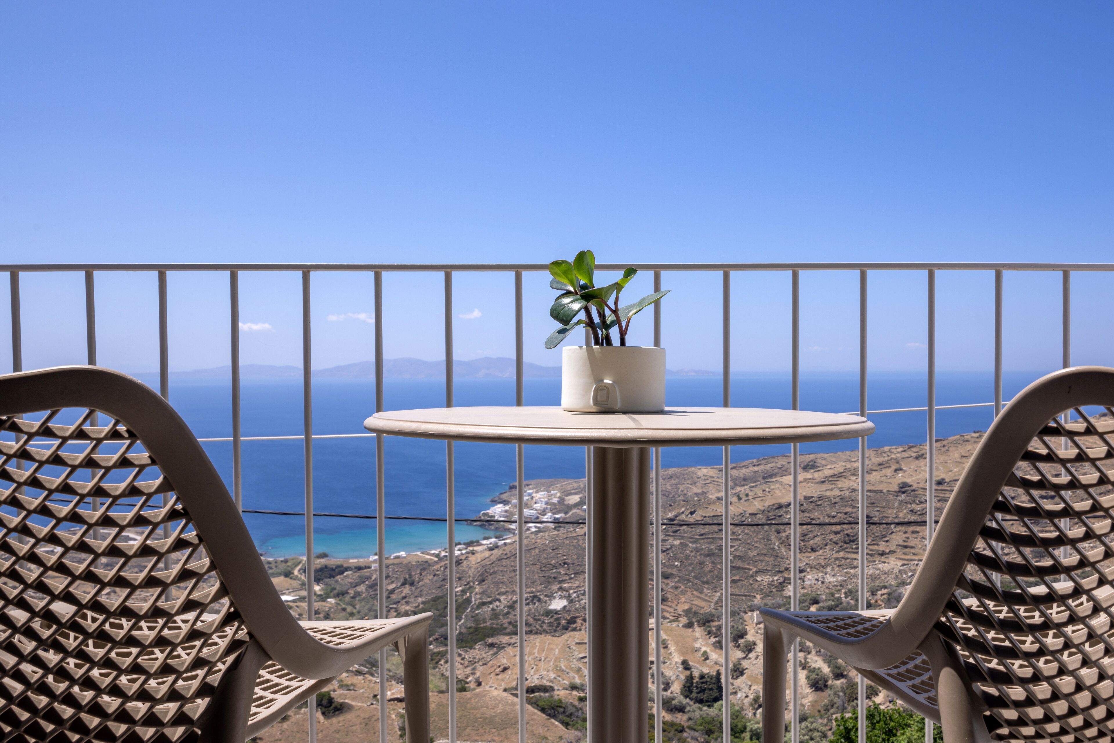 A balcony with a table and chairs, overlooking a coastal landscape.